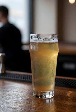 Social drinking and nightlife culture, glass of cold craft beer on a wooden bar counter in a pub with blurred background and relaxed atmosphere
