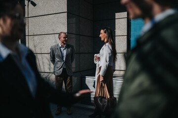 A man and woman in professional attire converse near a modern office building. Two blurred...