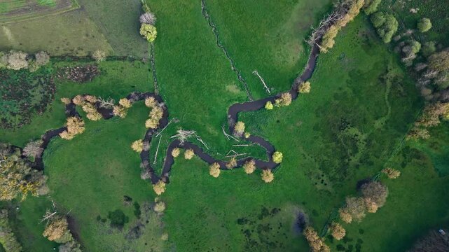 Meandering river across green countryside, seen from top down drone view. Landscape pattern in rural Normandy