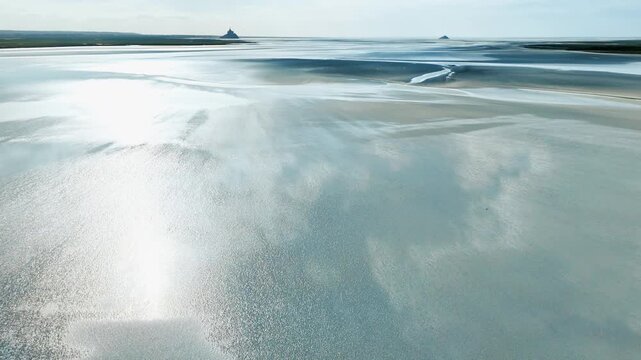 Tidal bay landscape on the Normandy coast with exposed flats, pale sand textures and shallow reflective water