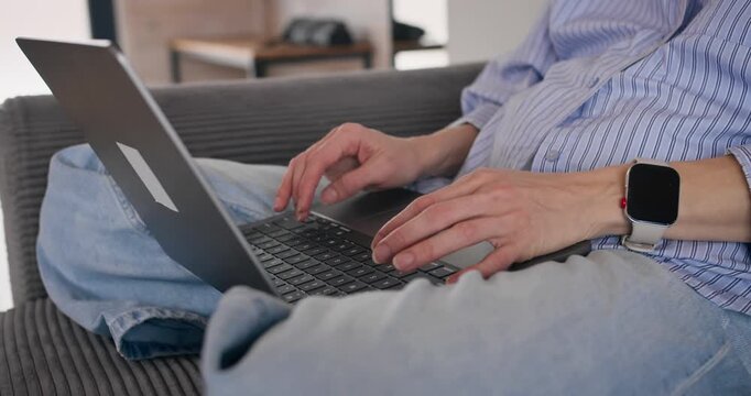 Close-up of woman hands typing on laptop keyboard while working from home on sofa.
