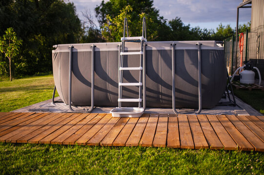 A frame pool with a ladder on the lawn in a backyard relaxation area during summer. Water treatment equipment, including a filter and pump.