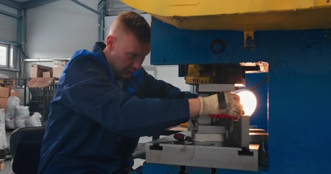 Press operator working with gloved hands around stamping die. Mechanical press tooling and hands-on industrial work in metalworking workshop