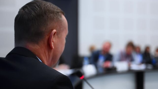 Rear view of a conference speaker addressing an audience at a professional event. Universal concept of public speaking, business communication, presentation and discussion.