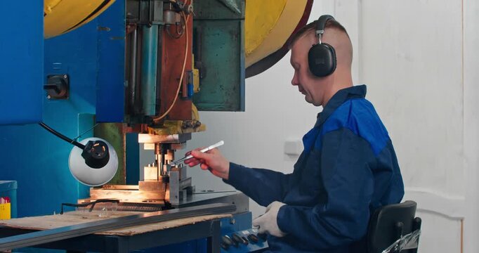 Factory worker at mechanical stamping press during metal parts bending. Medium shot of blue collar labor in component production