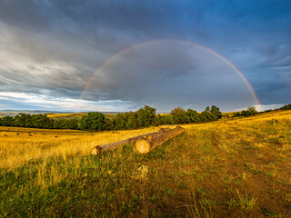 Obraz premium Faint Rainbow Beneath Dramatic Storm Clouds After Rain at Sunrise