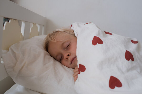  girl rubbing eyes waking up in cozy bed under duvet with red hearts