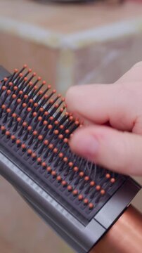 A hand picks loose hair strands out of a bristle hairbrush with copper handle, demonstrating brush cleaning and personal grooming maintenance.