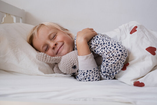  girl rubbing eyes waking up in cozy bed under duvet with red hearts