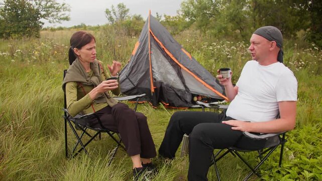 Man and woman unwinding together beside tent. Camping in nature and taking time away from everyday routine