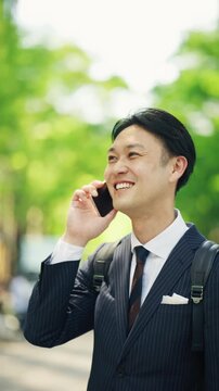 Smiling businessman on a hands free call under street trees in Tokyo