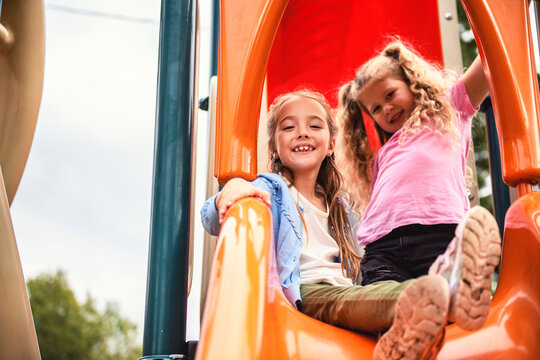 two Little girls on a slide outdoors in a park