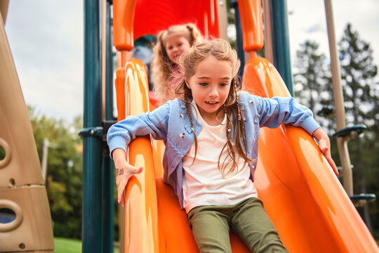 two Little girls on a slide outdoors in a park. the clid is a little bit afraid