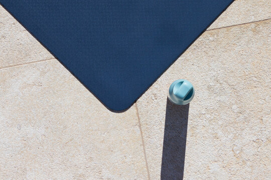 pale aqua cap is resting on sunlit patio tiles near navy mat corner, casting long shadow