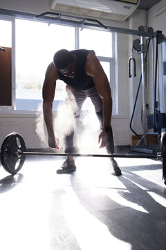 African American man wearing black tank top, shorts bending over loaded barbell at gym