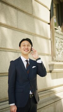 Businessman smiling during a phone call by a historic stone wall