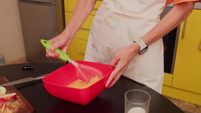 Close-up of woman mixing batter with whisk in home kitchen. Preparing homemade food by hand