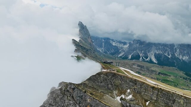 Fog moving across Seceda ridge with steep cliffs and hiking trail, aerial view, South Tyrol, Italy