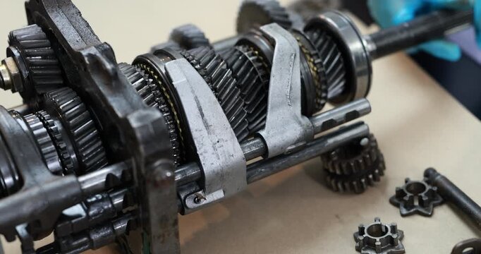 Close-up of disassembled manual transmission gears and shafts on a workshop bench, worn metal parts, bearings and small gear components during vehicle repair.