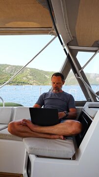 Focused man working on laptop aboard a sailing yacht. Productive remote office in a unique travel environment.