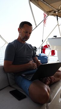 Thoughtful man sitting with laptop on a sailing yacht during a work break. Business planning and location independent lifestyle concept.