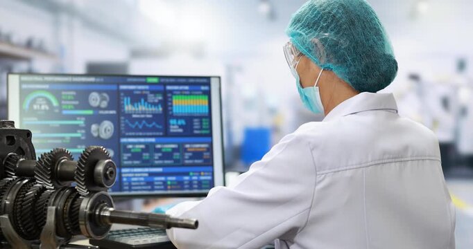 Technician in protective clothing monitors machine data on a computer beside industrial gears in a clean modern factory.