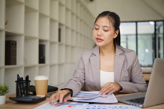 Asian businesswoman comparing financial documents at her office desk.