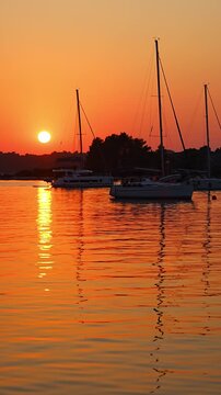 Sailing yachts anchored in a calm bay during a colorful summer sunset over the sea. Peaceful evening, golden hour, coastal travel destination and relaxing sailing lifestyle.