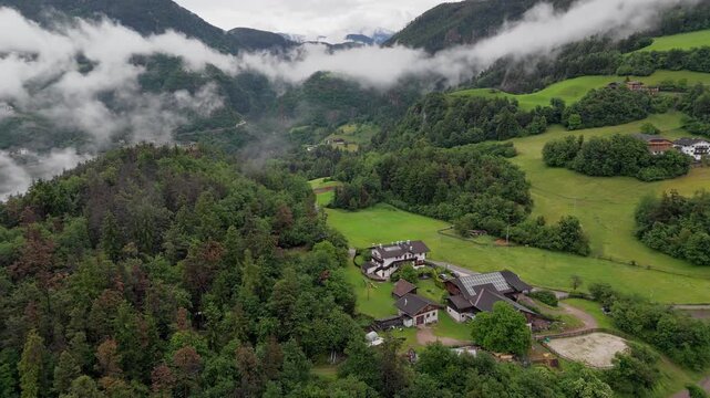 Farmhouses on village outskirts above misty mountain valley in Dolomites, South Tyrol, Italy. Aerial view of dolomites alps