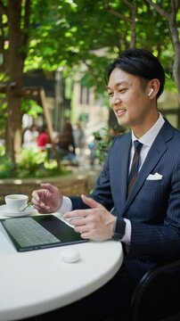 Japanese businessman in an online meeting with earphones at an outdoor cafe
