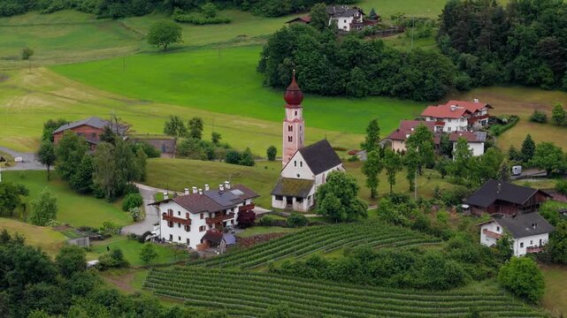 Church tower rises above village houses beside green farmland in Dolomites, South Tyrol, Italy