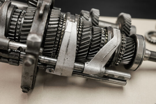 Close-up of a disassembled manual transmission gearbox with metal gears, shafts and bearings on a workbench.
