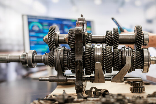 Close-up of an exposed manual transmission gearbox with metal gears and shafts in an automotive repair workshop.