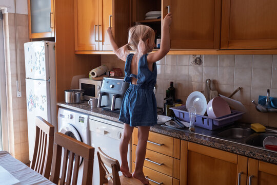 Little girl standing on chair reaching for top kitchen cabinet