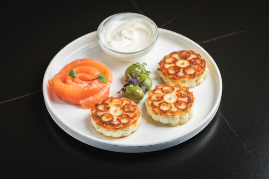 Savory Syrniki with Smoked Salmon, Olives and Sour Cream on White Plate