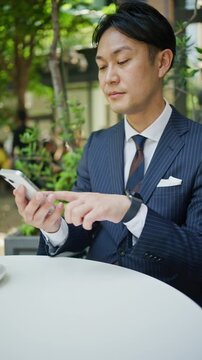 Businessman checking his smartphone at a cafe table under fresh green trees