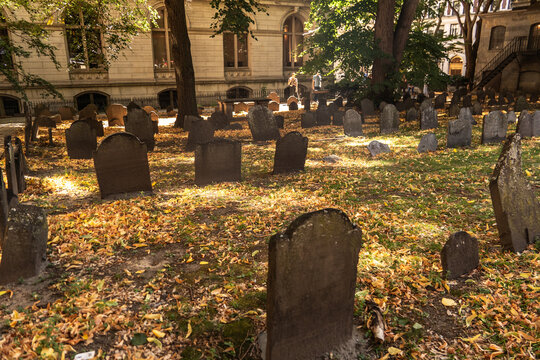 Historic city graveyard with weathered headstones under autumn trees and sunlight