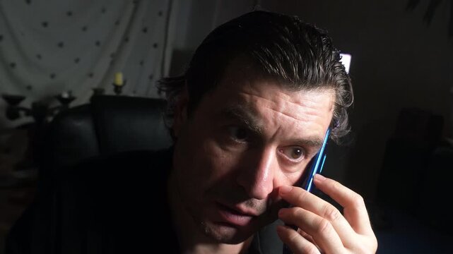 A man is talking on the phone, afraid of being overheard. He is frightened and glances around timidly.
