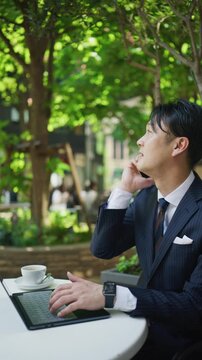 Japanese businessman taking a call while working at a cafe terrace