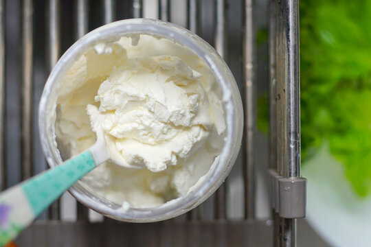 Greek yogurt in a clear plastic container with a spoon, top view.