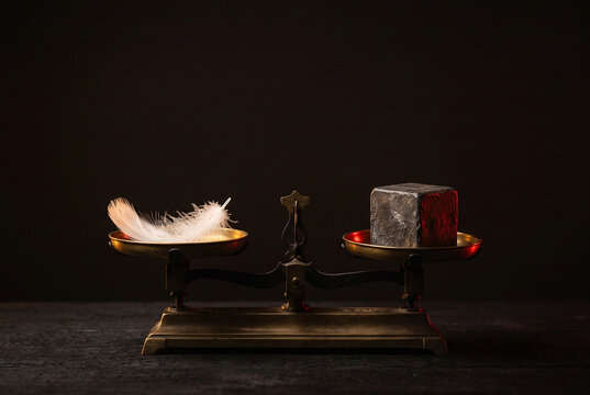 Balance scale with a feather against a heavy lead cube