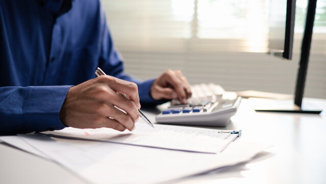 Business professional reviews financial documents and calculates audit figures. The scene represents accounting, tax audit, compliance, financial analysis, verification, and business reporting.
