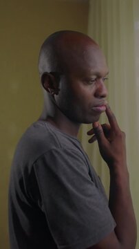 African American man holding jawline in modern living room expressing meticulous life planning deep analytical reasoning and serene domestic focus