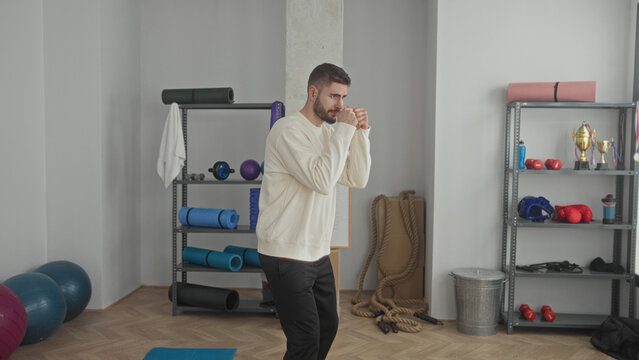 Man shadowboxes with fists in a fitness studio, throwing jabs and working footwork among mats and ropes; training determination.