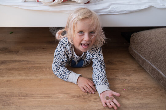 Joyful little girl lying on floor showing found coins under bed