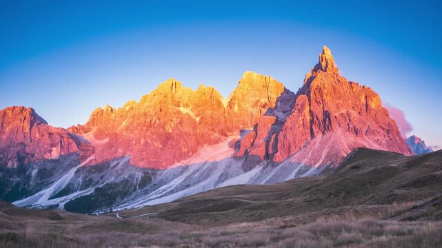 Time lapse: sunset illuminates Cimon della Pala and Pale di San Martino, Dolomites, Italy, casting vivid golden and pink light across dramatic rock spires and a tranquil mountain landscape
