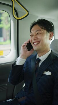Smiling Japanese businessman on a phone call in the back of a taxi