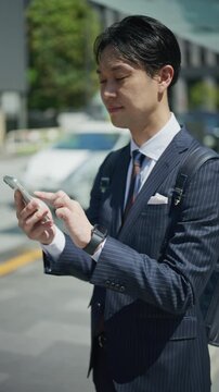 Japanese businessman reading a message on his phone beside a city street