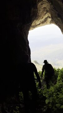 Silhouettes of Three Climbers Walking Toward Cave Exit Overlooking Mountain Cliff at Sunset