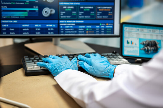 Scientist wearing blue gloves types on a keyboard at a laboratory desk with computer screens showing data, analysis charts and a technical image.